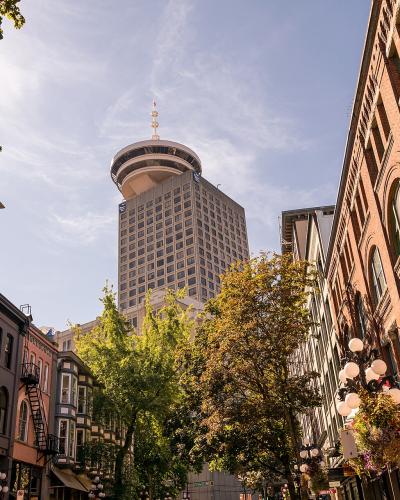A low-angle street view of historic brick buildings and cobblestones with the distinctive Vancouver Lookout tower rising in the background.