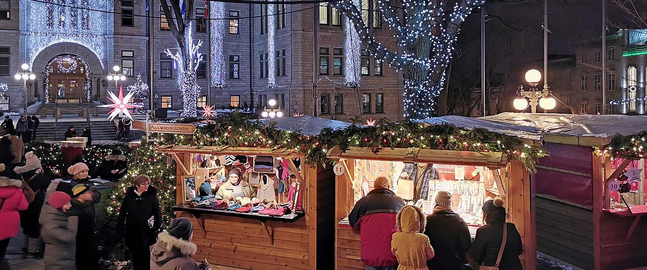 Wooden Christmas market stalls and lit trees in front of Québec City Hall at night