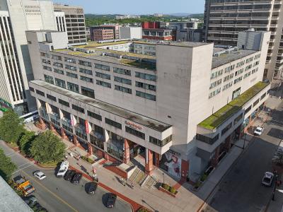 An aerial view of a large, multi-story commercial building complex featuring a "Lawtons Drugs" storefront and a "New Brunswick" banner on the facade, situated in an urban downtown area.