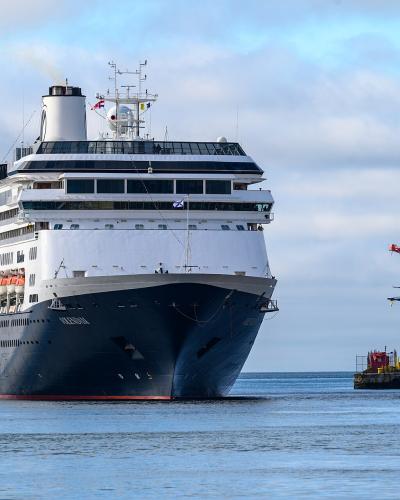 A large white and blue cruise ship named "VOLENDAM" is shown in the water near a dock with red industrial cranes.