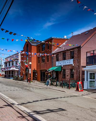A street scene showing a row of brick buildings with colorful bunting strung overhead, including a sign for "King of Spades" and a Canadian flag banner.