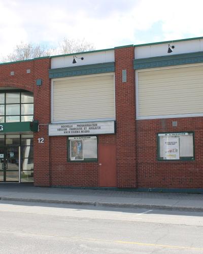 A red brick building with a green awning displaying the text "CINEMA MAGOG" above the entrance, situated on a street corner.