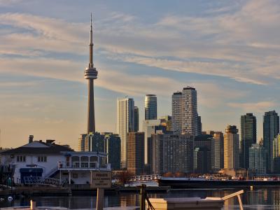 A view of the Toronto skyline featuring the CN Tower and high-rise buildings, viewed from across the water with a white building and a sign reading "PRIVATE G.T.Y.C. MEMBERS AND GUESTS ONLY" in the foreground.