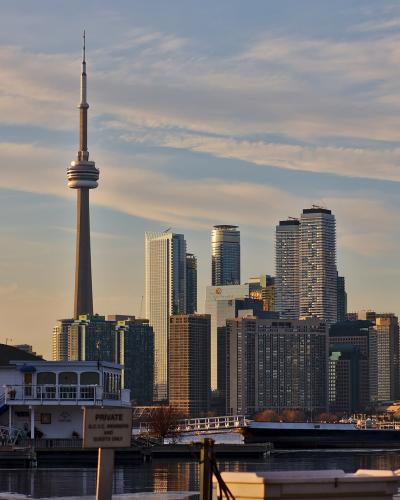 A view of the Toronto skyline featuring the CN Tower and high-rise buildings, viewed from across the water with a white building and a sign reading "PRIVATE G.T.Y.C. MEMBERS AND GUESTS ONLY" in the foreground.
