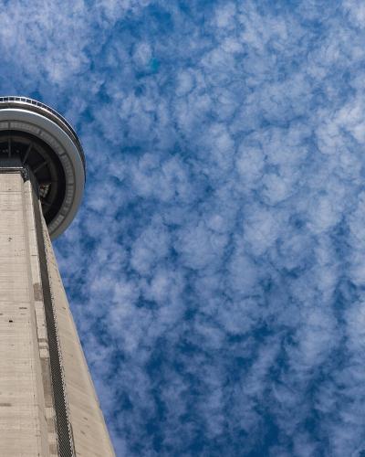 A low-angle shot looking up at the concrete shaft and pod of a tall telecommunications tower against a blue sky with scattered clouds.