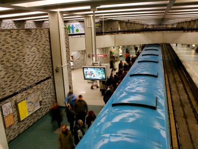 An interior view of a Montreal Metro station platform showing a blue train, tiled walls, and signage reading "PLACE-DES-ARTS".