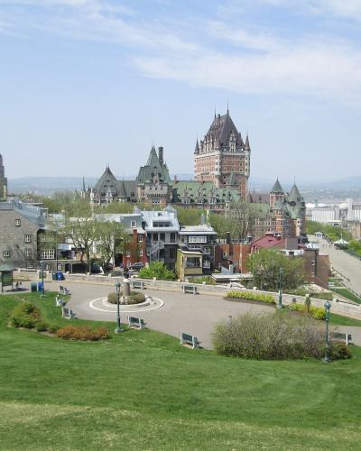 A high-angle view of the Quebec City skyline featuring the Château Frontenac, the Parliament Building, and the Dufferin Terrace, looking out over the St. Lawrence River.