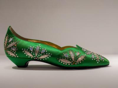 A side-profile studio photograph of an ornate green satin women's shoe decorated with silver and iridescent rhinestone floral motifs, displayed against a plain neutral background.